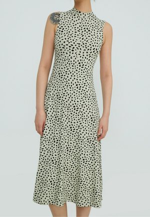 Sleeveless beige midi dress with small irregular black spots worn by person with sun face tattoo on upper arm.