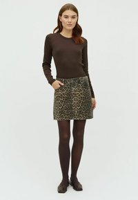 Un top lung maro cu mânecă lungă asociat cu o fustă din denim cu imprimeu de leopard. Fusta are o talie ajustată și două buzunare frontale. Ciorapi opaci maro și încălțăminte.