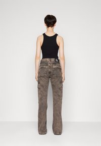 Camiseta sin mangas negra combinada con pantalones cargo de tiro alto y corte holgado. Los pantalones cuentan con múltiples bolsillos y un color marrón desgastado con un acabado texturizado.