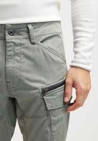 Ljusgrå cargobyxor med en zippered ficka, med en strukturerad tyg, snedställda sömmar och en standard knäppning.