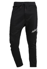 Zwarte tapering joggingsbroek met elastische tailleband, trekkoord, zijzakken met rits en witte cursieve tekst op het rechterdijbeen.