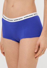 Μπλε βαμβακερό hipster εσώρουχο με λευκή ελαστική ζώνη που φέρει μαύρο κείμενο "BJÖRN BORG". Λείο υλικό και εφαρμοστή σχεδίαση.