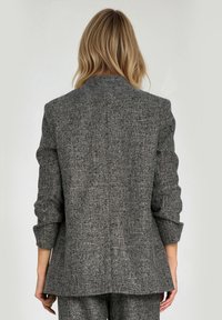 Teksturowany szary żakiet o dopasowanym kroju, z pojedynczym rozporkiem z tyłu i lekko podwiniętymi rękawami. Posiada klasyczny kołnierz i czyste linie.