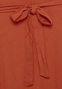 Látka v rezavé barvě s jemnou texturou, zdobená vázanou mašlí v pase a s pečlivým zakončením, vhodná na šaty nebo top.