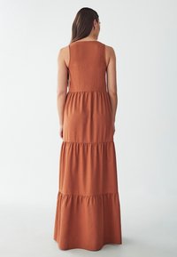 Vestido maxi largo y en capas de color óxido, con una textura suave. Presenta un diseño sin mangas y un sencillo escote redondo.