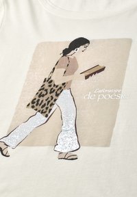 Woman with black hair walking while reading a book, wearing white pants, sandals, beige top, and carrying leopard print shoulder bag.
