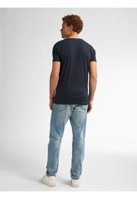 Tricou bleu marin cu mânecă scurtă și guler rotund, asortat cu blugi bleu deschis și adidași albi, văzut din spate.