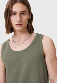 Olivgrünes geripptes Tanktop mit weitem Ausschnitt und ärmellosem Design. Das Modell trägt eine silberne Kettenhalskette und zeigt eine Nahaufnahme.
