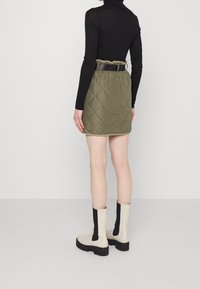 Jupe mini en olive matelassé avec une taille froncée, associée à des bottines crème et noires. Design simpliste, texture lisse.