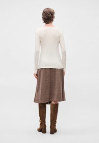 Hosszú ujjú, bordázott krémszínű felső, amelyet térd alá érő barna szoknyával párosítottak. Térd fölé érő barna velúr csizmák, vastag sarokkal és arany csat részletekkel.