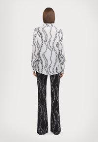 Λευκή μπλούζα με μακριά μανίκια και μαύρο μοτίβο αλυσίδας, συνδυασμένη με μαύρες φαρδιές παντελόνες με παρόμοιο σχέδιο. Λείο ύφασμα, άνετη εφαρμογή.