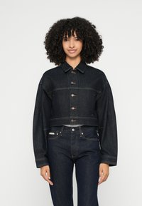 Krótka kurtka dżinsowa w ciemnym niebieskim kolorze z zapięciem na guziki, oversize'owymi rękawami i dwoma kieszeniami na piersiach. Gładka faktura i klasyczny design dżinsu.