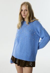 Blauwe, fuzzy gebreide trui met ronde hals, lange mouwen en versierd met metalen sterren en studs voor decoratieve accenten.