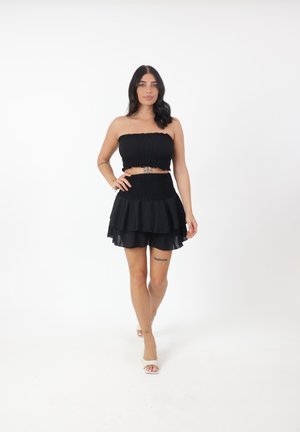 Completo nero a due pezzi composto da un top senza spalline arricciato e una mini gonna a strati. I materiali presentano una texture liscia con un design aderente.