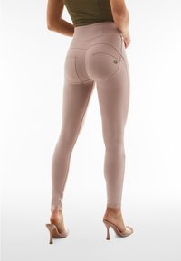 Leggings rosa cipria con vita alta, dotati di tasche posteriori curvate e lati senza cuciture, abbinati a sandali con tacco trasparente.