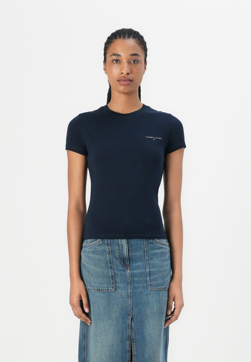 T-shirt fitted a maniche corte di colore navy, realizzato in cotone, con un piccolo logo bianco sul petto e una texture liscia. Abbinato a una gonna di jeans.