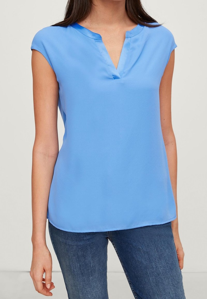 Helles blaues Kurzarmbluse mit V-Ausschnitt und glatter, leichter Textur. Kombiniert mit lässigen blauen Jeans.