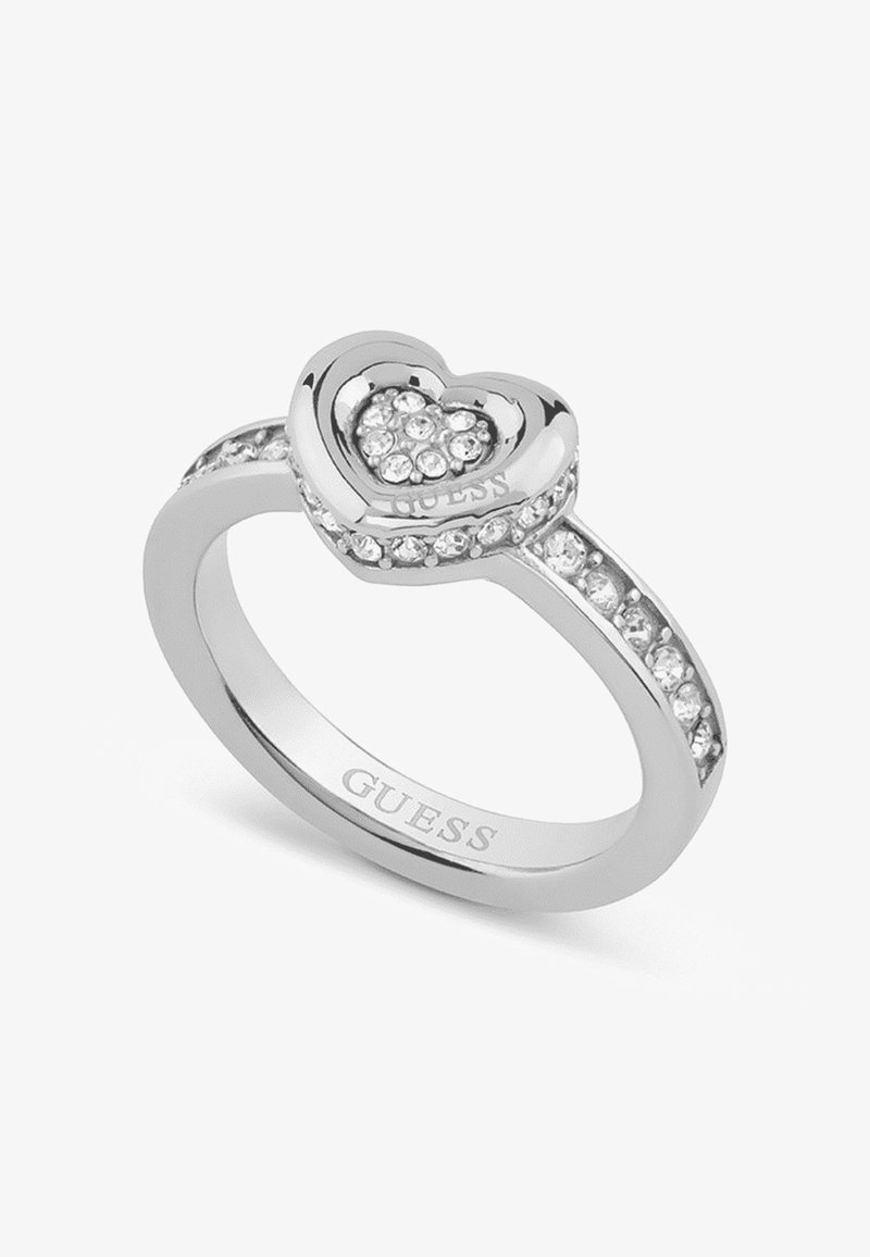 Srebrny pierścionek z motywem serca, ozdobiony małymi przezroczystymi kamieniami, wygrawerowany napisem "GUESS" oraz zaakcentowany rzędem kamieni na obrączce.
