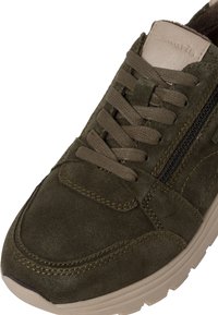 Sneaker scuro verde in suede con design lacci, zip laterale, dettagli marroni e suola in gomma beige. Texture liscia con cuciture a vista.