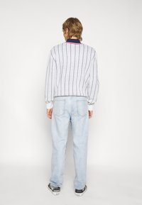 Suéter gris claro con cuello azul marino y rojo, con rayas verticales. Combinado con jeans azul claro y zapatillas en blanco y negro.