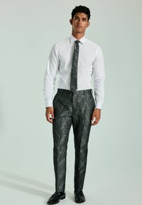 Hvid skjorte parret med sorte bukser med et sølvblad mønster. Outfittet er afsluttet med et matchende slips og sorte sko.