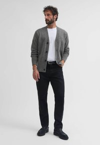 Cardigan gris de punto con cierre de botones, usado sobre una camiseta blanca, combinado con pantalones negros y zapatos negros, que presenta un ajuste relajado.