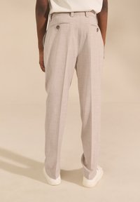 Pantaloni grigi chiaro su misura con una finitura testurizzata, dotati di due tasche posteriori con bottoni e taglio dritto, abbinati a sneakers bianche.