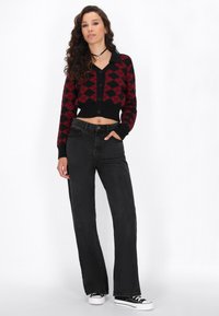 Čierny a červený kardigán s károvaným vzorom, skrátený a s gombíkmi, v kombinácii s vysokými čiernymi džínsami a čiernymi teniskami.