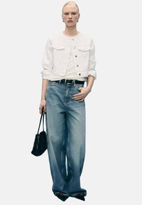 Bílá džínová bunda přes bílý top, doplněná světle modrými oversized džíny. Celkový look doplňují černá kabelka a černé špičaté boty.