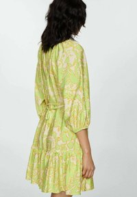 Rochie florală în nuanțe de verde și bej, cu modele contrastante de portocalie. Dispune de mâneci bufante și o tiv ruffled. Fabricată dintr-un material ușor.