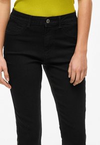 Mustat farkut slim fit -mallilla, joissa on etutaskut, metallinen nappikiinnitys ja huomaamattomia ompeluyksityiskohtia. Pehmeä pinta ja klassinen muotoilu.