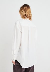 Weißes Langarmhemd aus Baumwolle mit Button-down-Kragen, Rückenpasse und abgerundetem Saum. Verfügt über Knopfmanschetten und eine lockere Passform.
