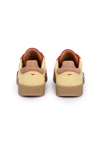 Gelbe Leder-Sneaker mit roten Akzenten, ausgestattet mit einer braunen Fersenplatte und einer strukturierten Gummisohle. Die Rückansicht zeigt das Branding auf der Ferse.