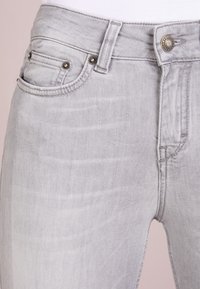 Jeans in denim grigio chiaro dal design aderente, con chiusura lampo, bottone metallico e cinque tasche con cuciture decorative.