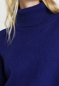 Maglione a collo alto blu navy realizzato in un morbido tessuto lavorato. Presenta un colletto a coste e un corpo liscio per una vestibilità confortevole.