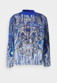 Blå og hvit mønstrete bomberjakke med intrikate grafiske designs, elastiske mansjetter og midjebånd, med "Carlo Colucci"-logoen tydelig vist.