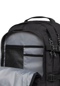 Intérieur d'un sac à dos noir avec doublure grise, présentant une poche en maille et plusieurs sangles d'organisation. Texture lisse avec fermetures éclair.