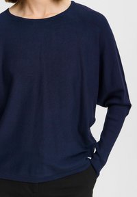 Pull en maille bleu marine avec un col rond, coupe ample et manches longues. Présente des poignets côtelés et une texture délicate.