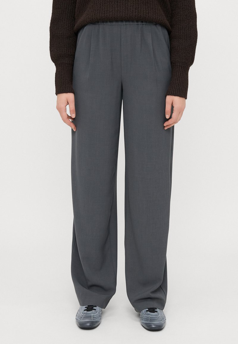 Graue weit geschnittene Hose mit flachem Frontdesign, elastischem Bund und leichtem Stoff. Dazu passende blau-graue Schnürschuhe.