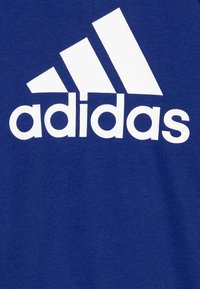 Camiseta de algodón azul con gran logo blanco de Adidas y tres rayas diagonales. Textura suave con un ajuste casual y relajado.