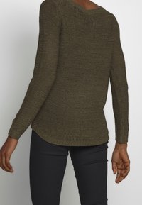 Khaki pletený svetr s volným střihem, dlouhými rukávy a kulatým lemem. Texturovaný materiál; měkký vzhled a žebrované manžety.