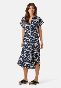 Navy Kleid mit weißem abstraktem Blumenmuster, kurzen Ärmeln, V-Ausschnitt, fließender Silhouette, seitlichen Schlitzen, kombiniert mit schwarzen Rutschlatschen.