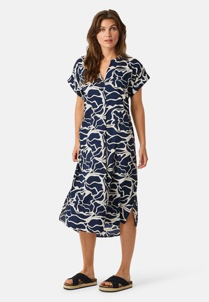 Navy Kleid mit weißem abstraktem Blumenmuster, kurzen Ärmeln, V-Ausschnitt, fließender Silhouette, seitlichen Schlitzen, kombiniert mit schwarzen Rutschlatschen.