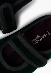 Zapatillas de terciopelo verde con ribete gris, con correas ajustables y un interior suave color púrpura, mostradas desde un ángulo cenital.