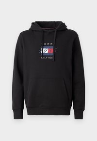 Sort hoodie med en frontlomme. Har et farverigt logo med "TOMMY HILFIGER" og "1985" i rød, hvid og blå. Fremstillet af bomuldsstof.