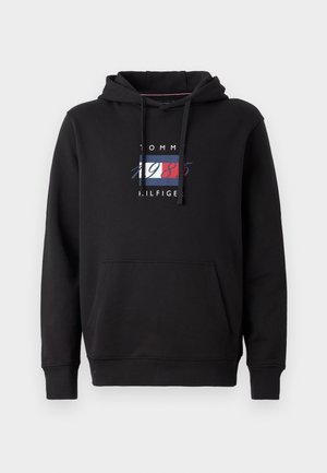 Zwarte hoodie met een voorzak. Heeft een kleurrijk logo met "TOMMY HILFIGER" en "1985" in rood, wit en blauw. Van katoen.