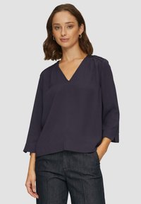 Navybluse mit V-Ausschnitt und Dreiviertelärmeln. Mit gerafften Details an den Schultern und einem lockeren, entspannten Schnitt. Glatte Stofftextur.