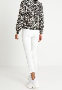 Bluse mit Leopardenmuster und langen Ärmeln, aus leichtem Stoff, mit Knopfdetails am Rücken; kombiniert mit weißen Skinny-Jeans und weißen Sneakers.