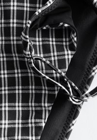 Zwart-wit geruit stof met verstelbare riem voorzien van een kleine zwarte gesp en gedetailleerde stiksels.