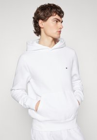 Sweatshirt à capuche blanche en coton avec une poche frontale. Doté d'un petit logo sur la poitrine et de poignets côtelés aux manches et à l'ourlet.